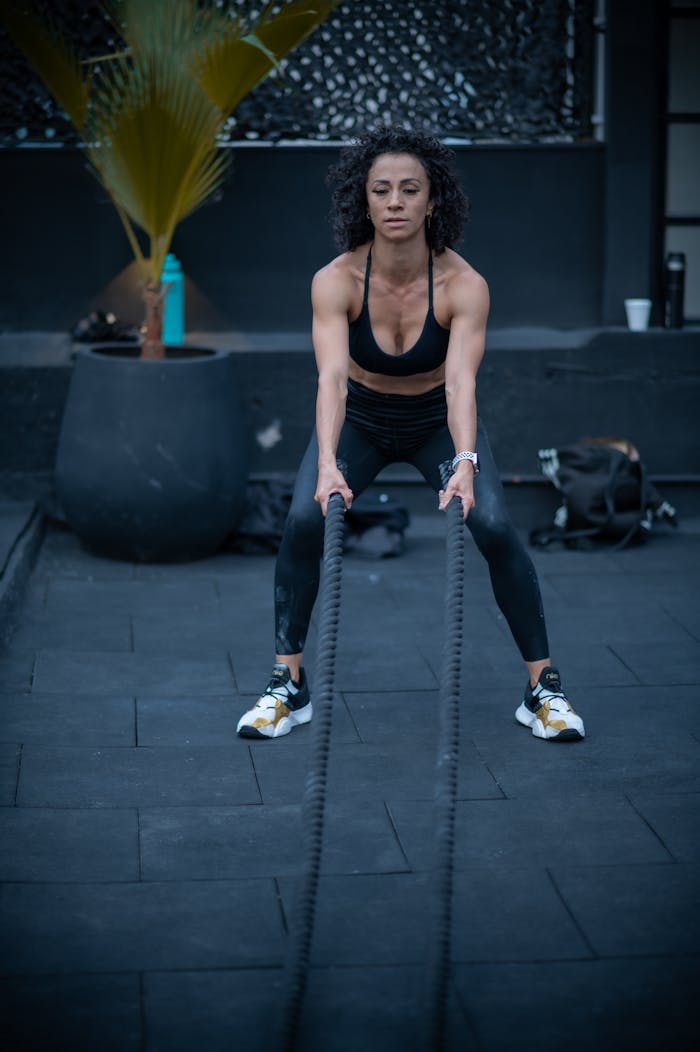 Athletic woman in sportswear working out with battle ropes outdoors in a fitness setting.