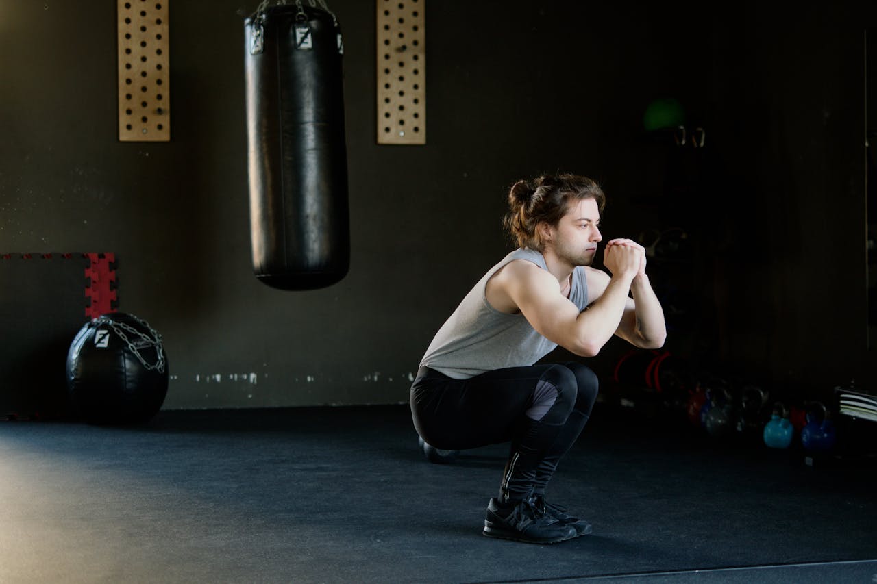 A man is doing squats in a gym with a punching bag. The setting appears stylish and focused on fitness.